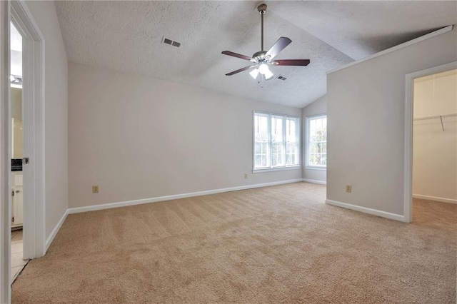 unfurnished bedroom featuring vaulted ceiling, a textured ceiling, light carpet, ceiling fan, and a spacious closet