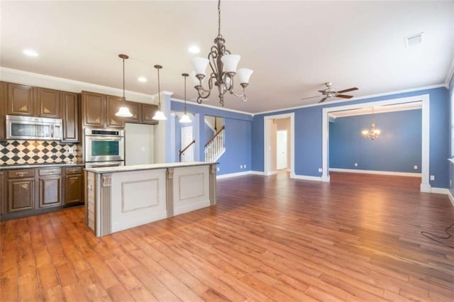 kitchen with appliances with stainless steel finishes, hanging light fixtures, backsplash, hardwood / wood-style floors, and a center island