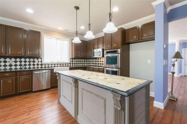 kitchen with pendant lighting, crown molding, appliances with stainless steel finishes, a center island, and light stone countertops