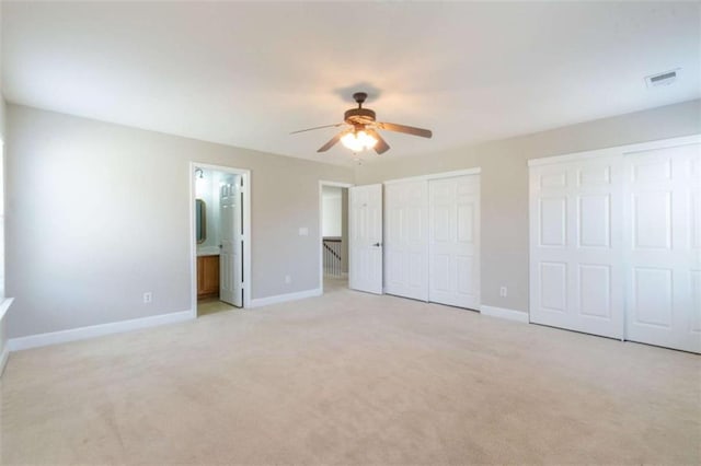 unfurnished bedroom with ensuite bathroom, two closets, light colored carpet, and ceiling fan