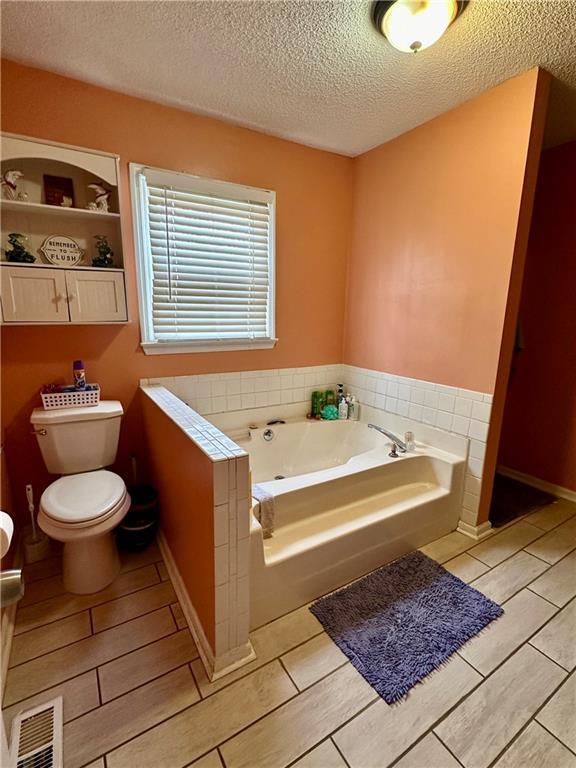 bathroom featuring a textured ceiling, a garden tub, toilet, wood finish floors, and visible vents