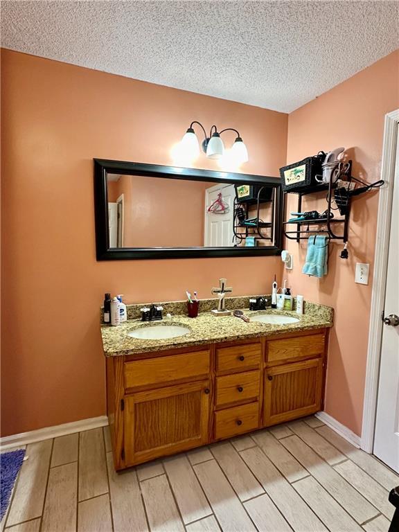 bathroom with double vanity, a textured ceiling, a sink, and wood finish floors