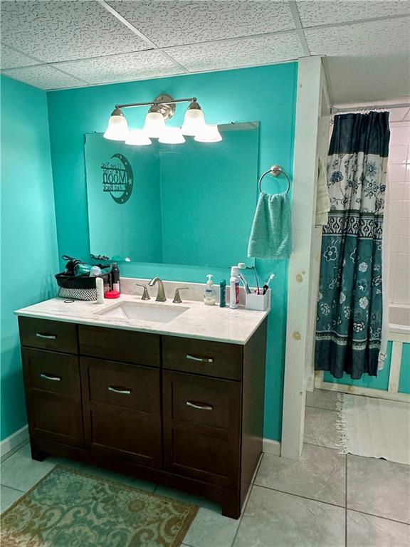 full bath with a drop ceiling, vanity, baseboards, and tile patterned floors