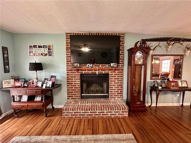 living area featuring a textured ceiling, a fireplace, wood finished floors, and baseboards