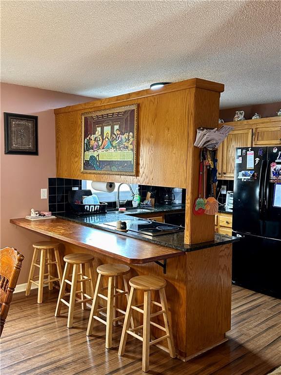 kitchen featuring dark countertops, light wood-type flooring, brown cabinetry, and freestanding refrigerator