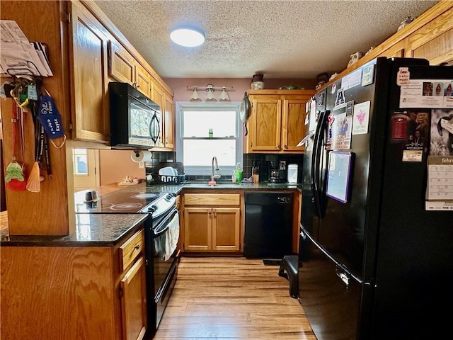 kitchen with a textured ceiling, a sink, light wood-style floors, black appliances, and brown cabinetry