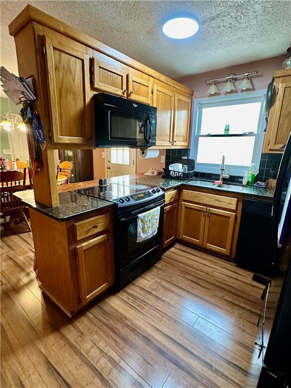 kitchen featuring a peninsula, black appliances, brown cabinetry, and light wood-style floors