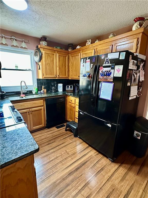 kitchen featuring brown cabinets, backsplash, light wood-style flooring, a sink, and black appliances