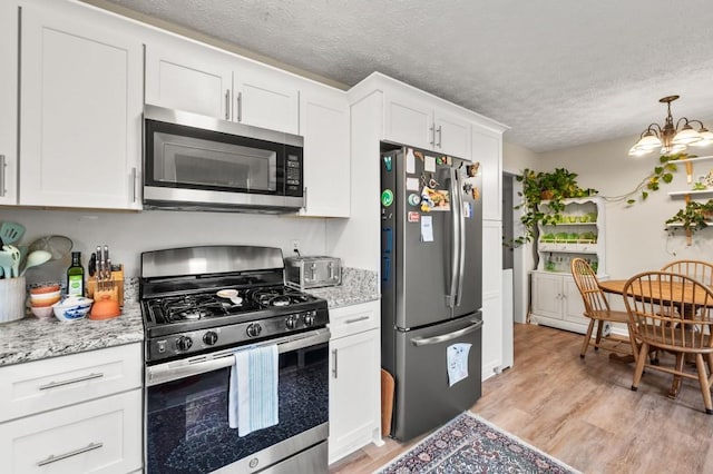 kitchen with white cabinetry, a chandelier, light stone counters, stainless steel appliances, and a textured ceiling