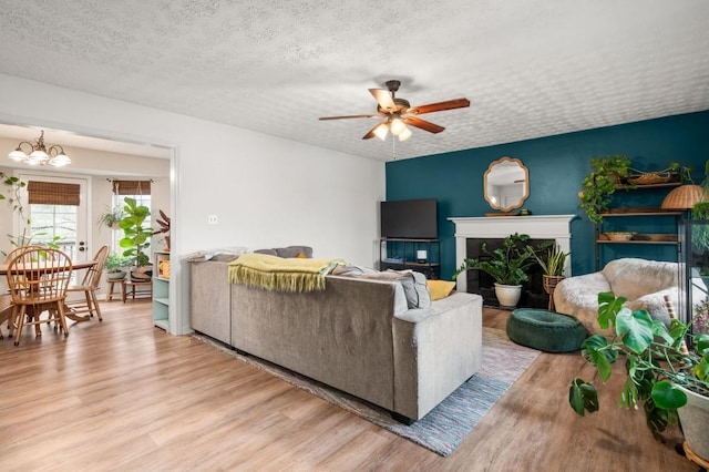 living room with ceiling fan with notable chandelier, a textured ceiling, and light wood-type flooring