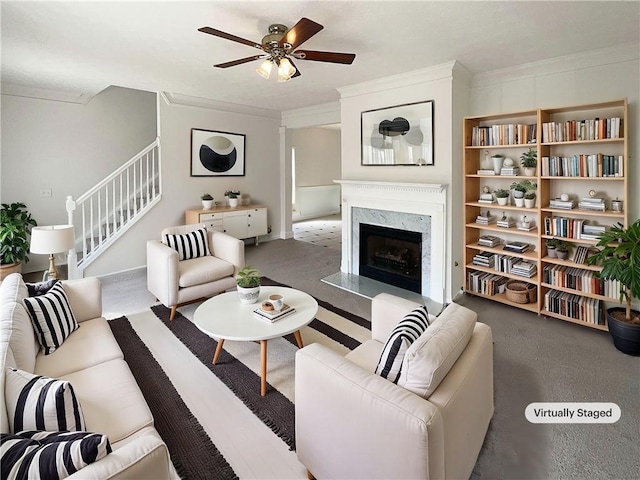 living area featuring ceiling fan, a premium fireplace, ornamental molding, and stairway