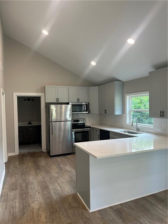 kitchen with wood-type flooring, kitchen peninsula, sink, backsplash, and appliances with stainless steel finishes