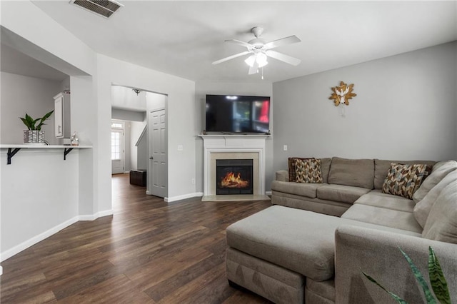 living area with dark wood-style flooring, a warm lit fireplace, a ceiling fan, baseboards, and visible vents