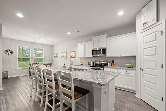 kitchen with a kitchen breakfast bar, sink, an island with sink, white cabinets, and appliances with stainless steel finishes