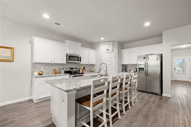 kitchen featuring an island with sink, white cabinets, a breakfast bar, light hardwood / wood-style flooring, and appliances with stainless steel finishes