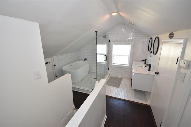 bathroom with vaulted ceiling, vanity, a freestanding tub, a shower stall, and tile walls