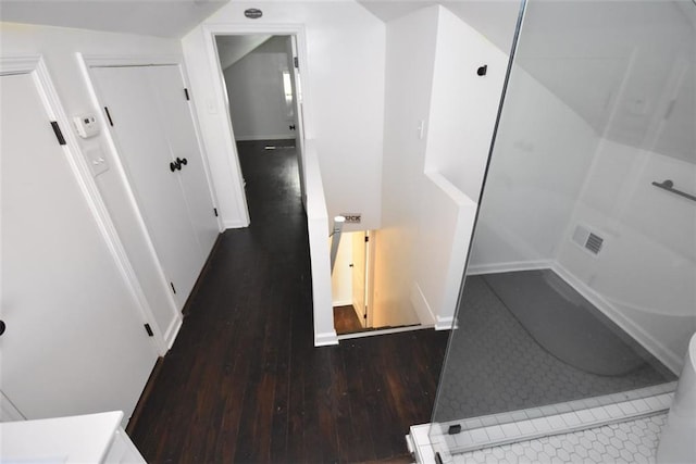 hallway featuring wood-type flooring, visible vents, baseboards, and an upstairs landing