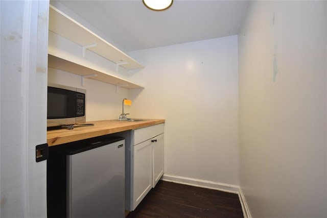 bar with stainless steel appliances, dark wood finished floors, a sink, and baseboards