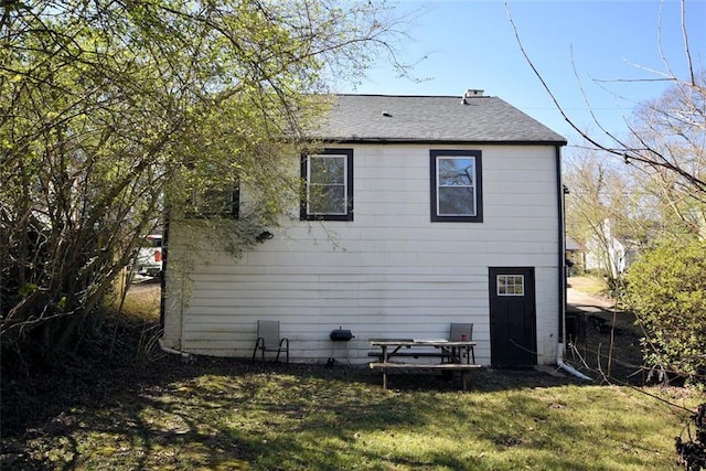 back of house featuring a shingled roof and a lawn