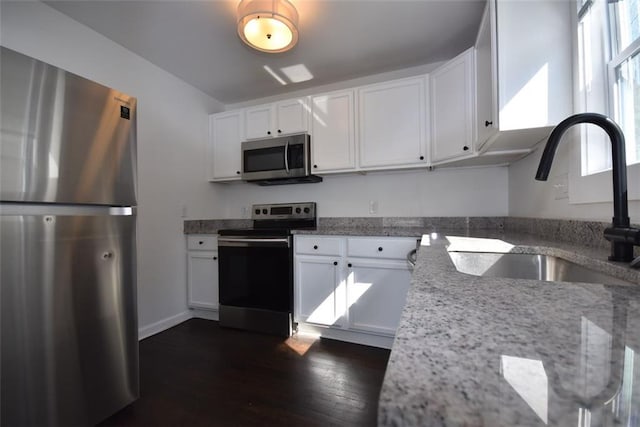 kitchen featuring stainless steel appliances, a sink, light stone countertops, and white cabinets