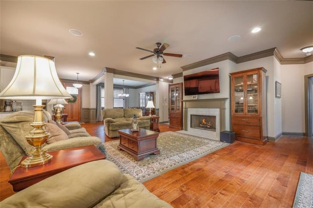 living room with ceiling fan with notable chandelier, ornamental molding, and light hardwood / wood-style floors