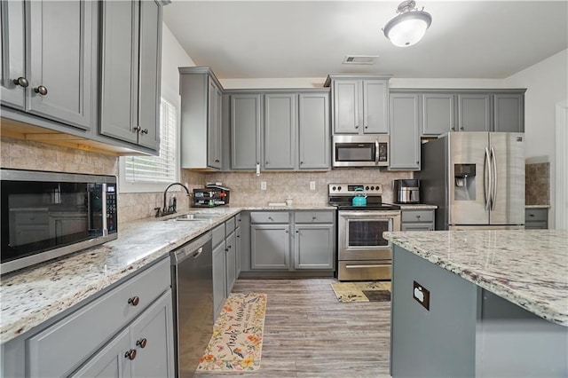 kitchen featuring visible vents, light stone countertops, gray cabinets, a sink, and stainless steel appliances