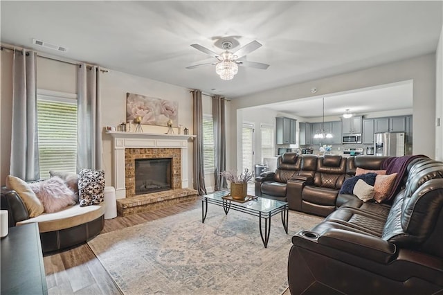 living area with ceiling fan, a brick fireplace, light wood-type flooring, and visible vents