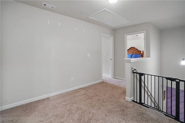 carpeted spare room with baseboards, visible vents, and attic access