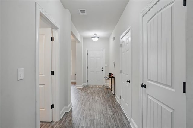 corridor with baseboards, visible vents, and wood finished floors