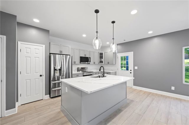 kitchen with appliances with stainless steel finishes, light stone counters, light wood-type flooring, and an island with sink