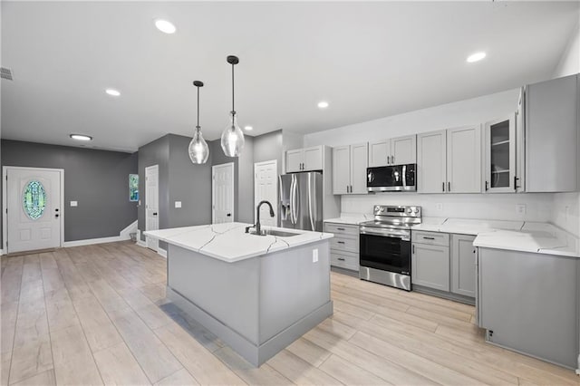 kitchen featuring a center island with sink, stainless steel appliances, sink, light hardwood / wood-style floors, and decorative light fixtures