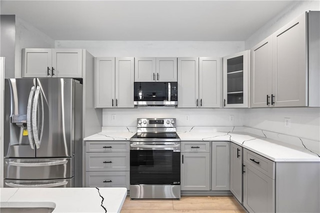 kitchen with gray cabinets, light stone counters, appliances with stainless steel finishes, and light hardwood / wood-style flooring