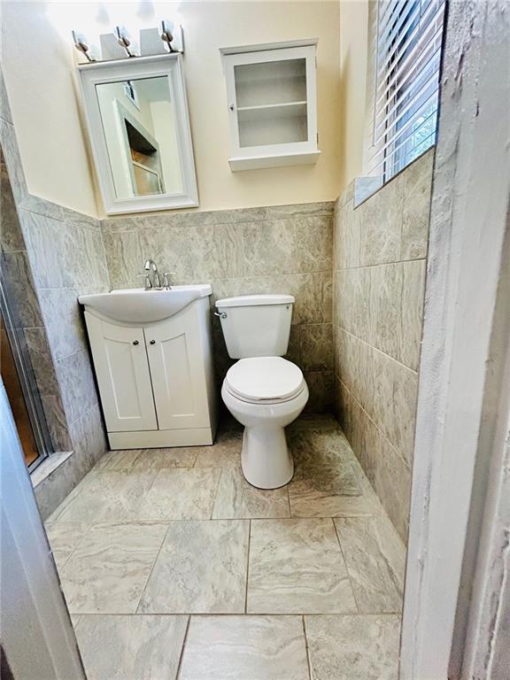 bathroom with tile walls, vanity, toilet, and tile patterned flooring