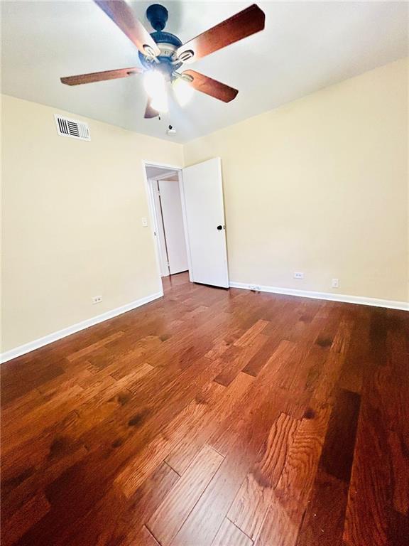 spare room with a ceiling fan, visible vents, baseboards, and wood finished floors