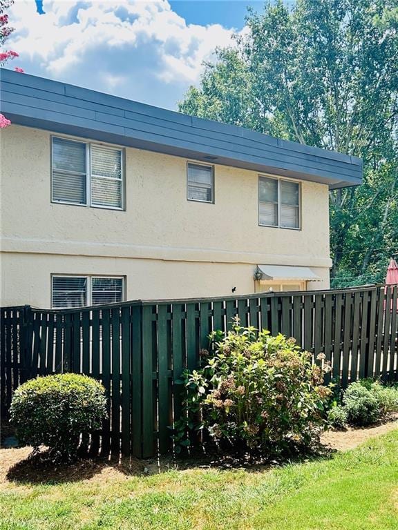 view of side of property with a lawn, fence, and stucco siding