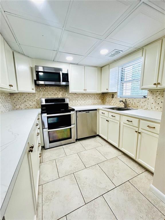 kitchen with appliances with stainless steel finishes, light tile patterned flooring, sink, and decorative backsplash