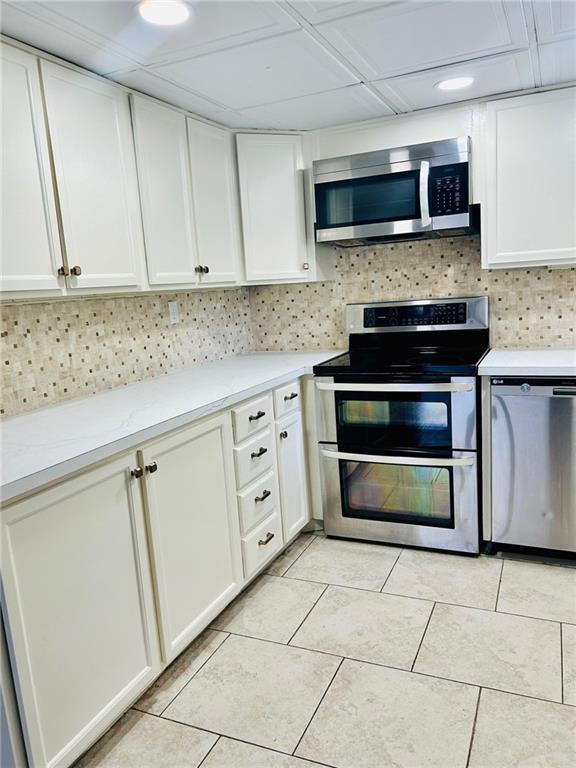 kitchen with light tile patterned floors, white cabinetry, light countertops, appliances with stainless steel finishes, and decorative backsplash