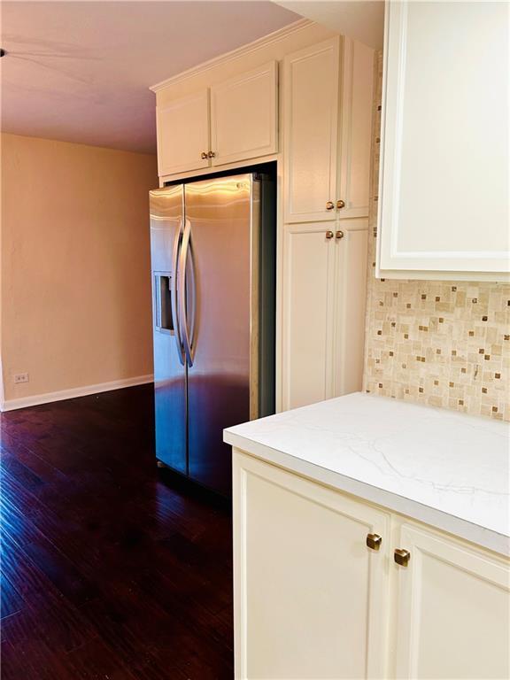 kitchen featuring dark wood-style floors, stainless steel fridge, white cabinetry, and decorative backsplash