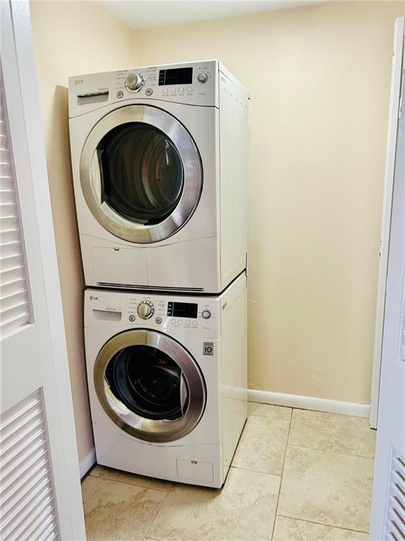 washroom featuring stacked washer / dryer, laundry area, baseboards, and light tile patterned floors