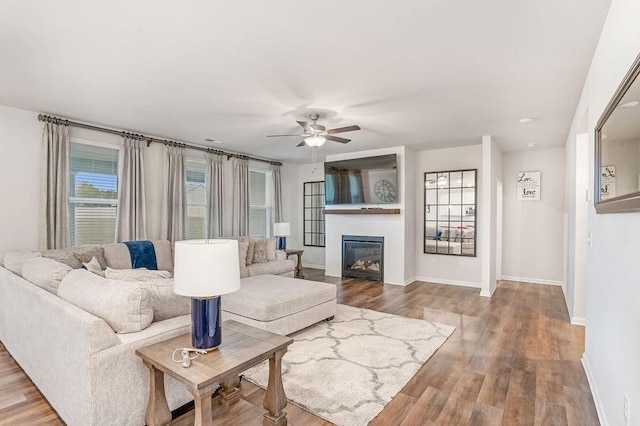 living room with a glass covered fireplace, baseboards, ceiling fan, and wood finished floors