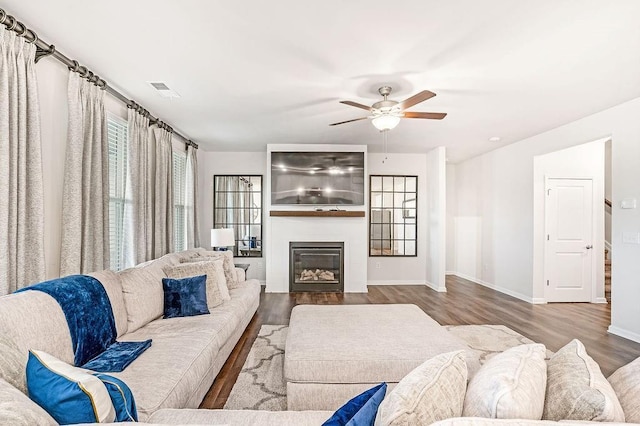 living area featuring baseboards, a ceiling fan, wood finished floors, and a large fireplace