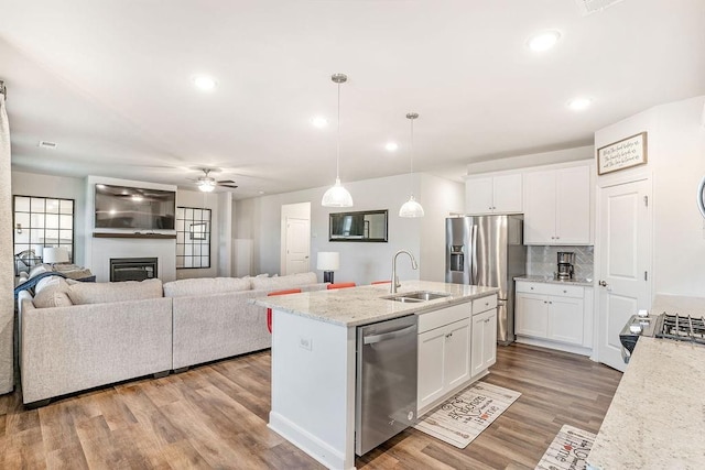 kitchen featuring a sink, stainless steel appliances, open floor plan, white cabinetry, and wood finished floors