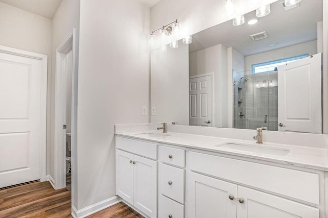 full bath featuring a sink, double vanity, a shower stall, and wood finished floors