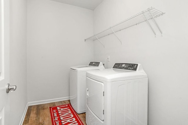 clothes washing area with washer and dryer, laundry area, baseboards, and wood finished floors