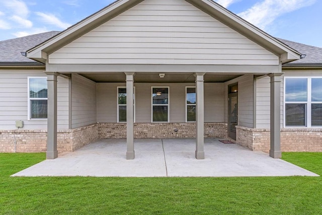 back of house with a lawn, a patio, roof with shingles, and brick siding