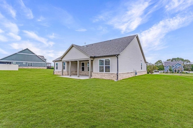 back of property with a yard, a patio, a shingled roof, and stone siding