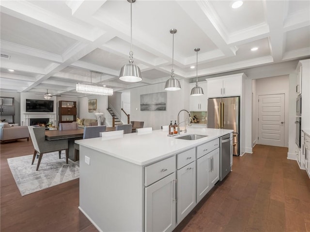 kitchen featuring hanging light fixtures, appliances with stainless steel finishes, a kitchen island with sink, dark wood-type flooring, and sink