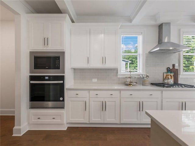 kitchen with appliances with stainless steel finishes, white cabinets, wall chimney range hood, and backsplash