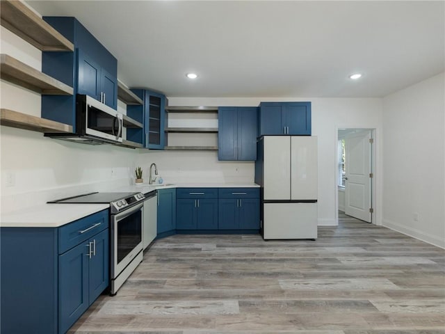 kitchen featuring appliances with stainless steel finishes, blue cabinetry, sink, and light wood-type flooring