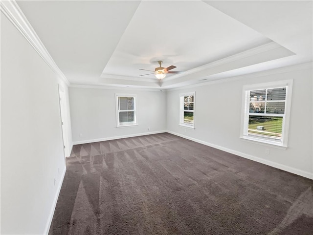 unfurnished room featuring ornamental molding, dark colored carpet, a raised ceiling, and baseboards